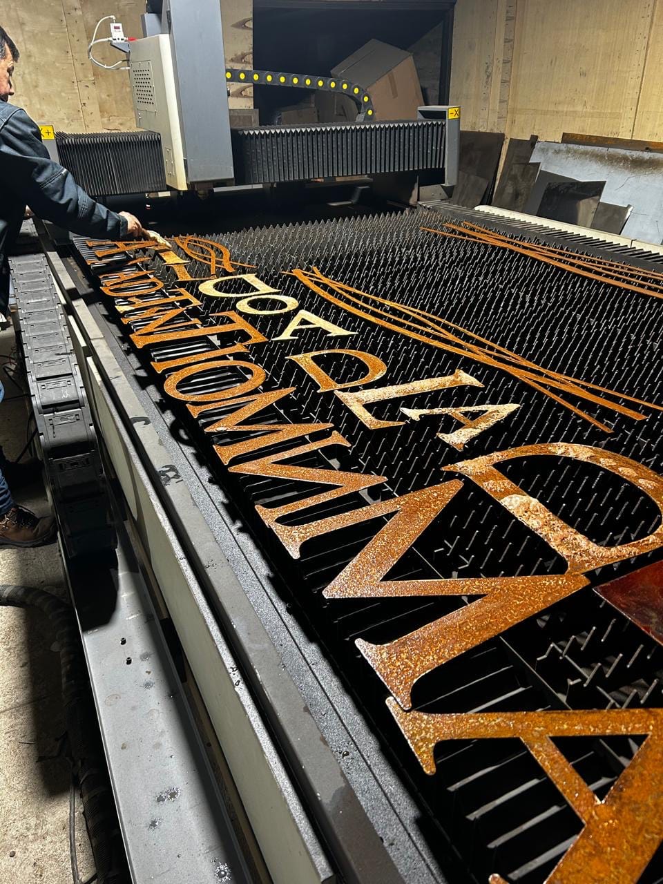 Trabajador retirando letras de acero color óxido recién cortadas de una mesa CNC