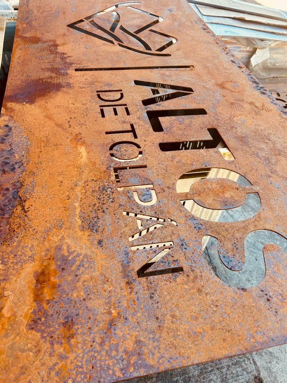 Detalle del nombre y símbolo de Altos de Tolpán cortados en una placa de acero envejecido